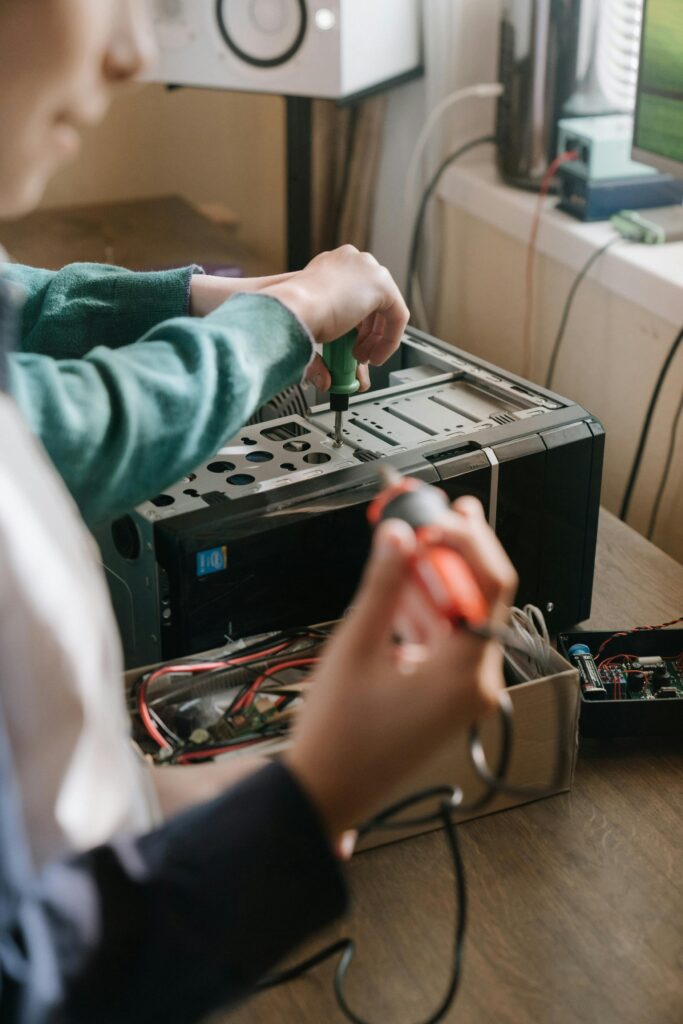 Adults working together to repair a computer using tools like a screwdriver and soldering iron.